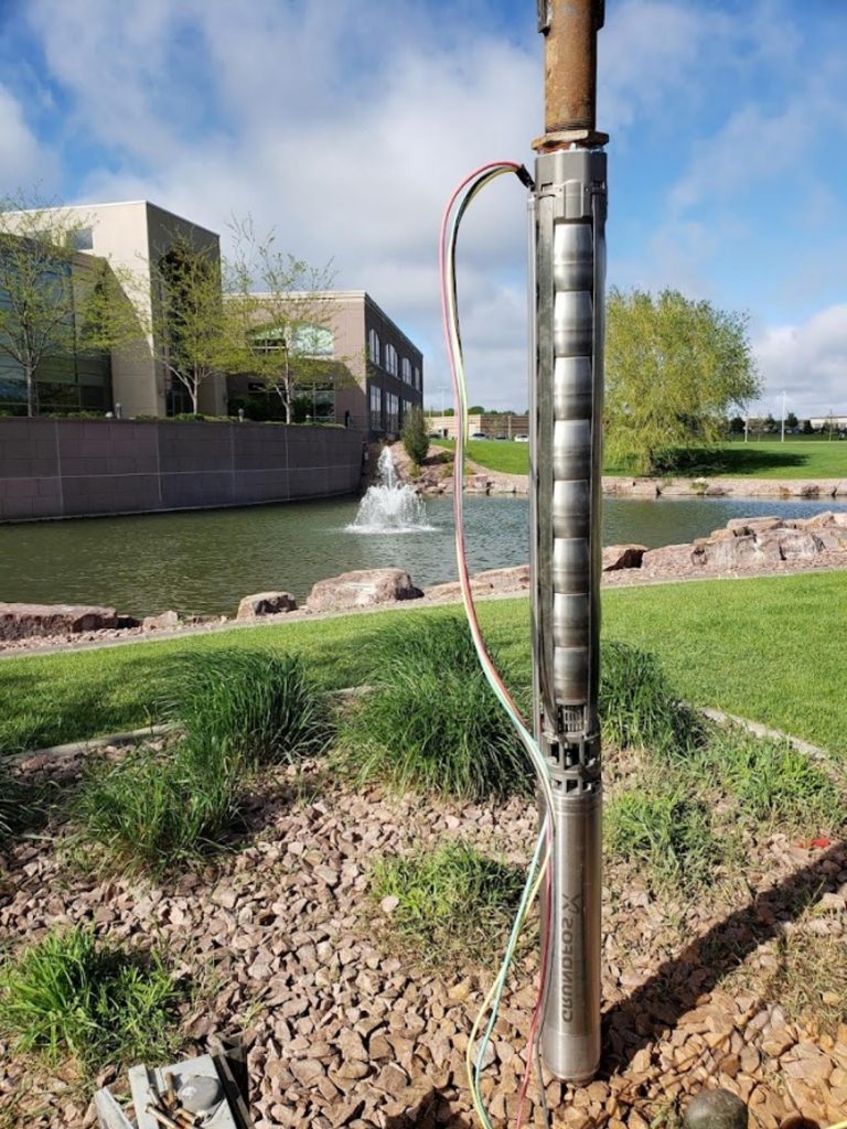 Submersible well pump completely removed from a water well near a landscaped pond.